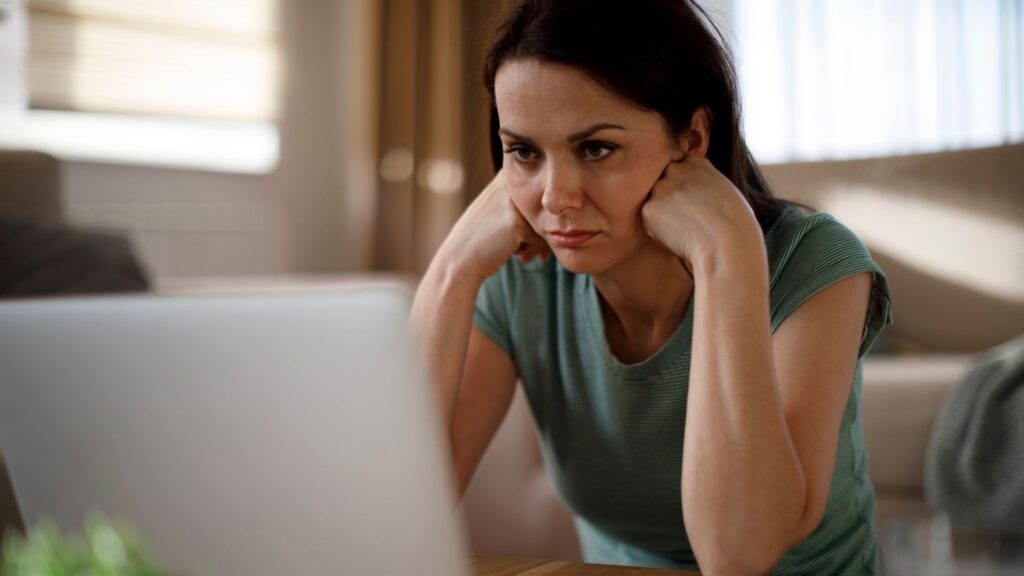 Is a W on Transcript Bad for Admissions Chances? 1 girl struggling with hands under chin, seems stressed out and has computer in front of her. Green top, dark haired
